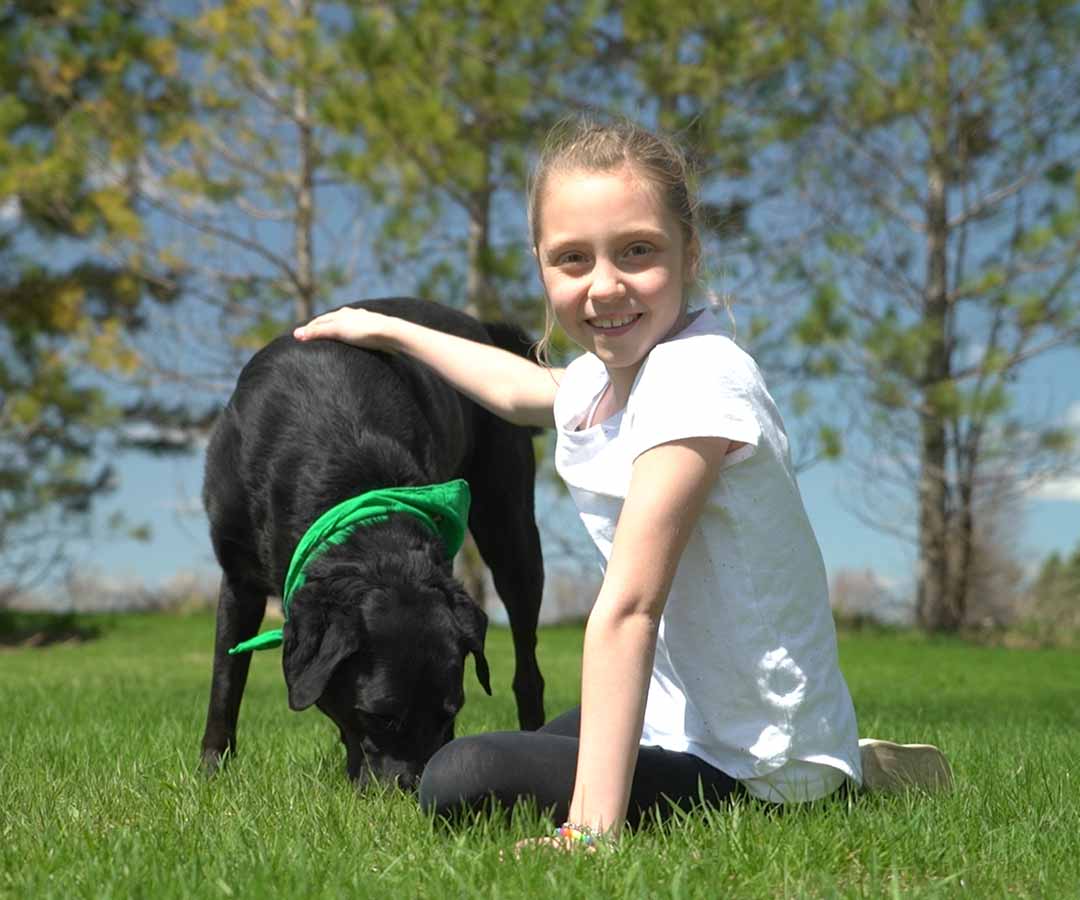 Happy girl playing with her black lab puppy on a freshly cut lawn.